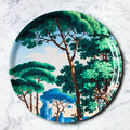 "Plateau décoratif rond motif paysage méditerranéen avec palmiers et architecture, fond turquoise"